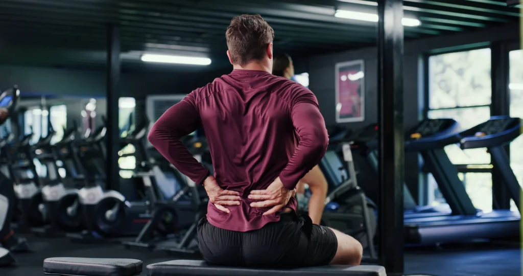 man sitting in gym holding lower back in pain 2026 06 08 16 54 09 utc