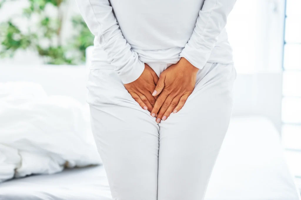 woman in white holding genital area medical conce 2026 03 17 05 03 22 utc