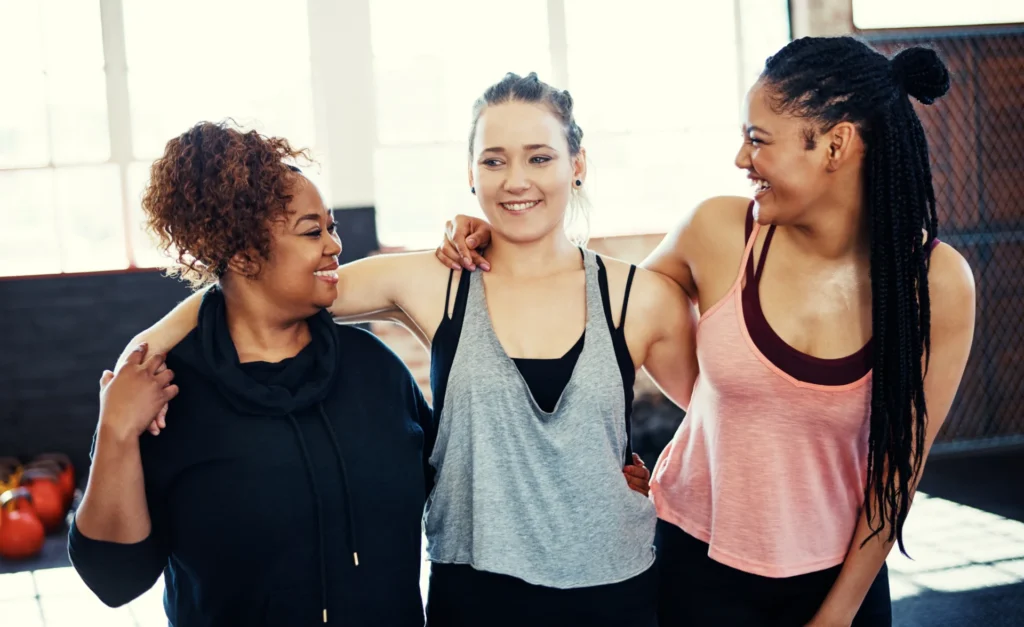three smiling women embracing in a bright gym sett 2026 09 25 04 04 55 utc